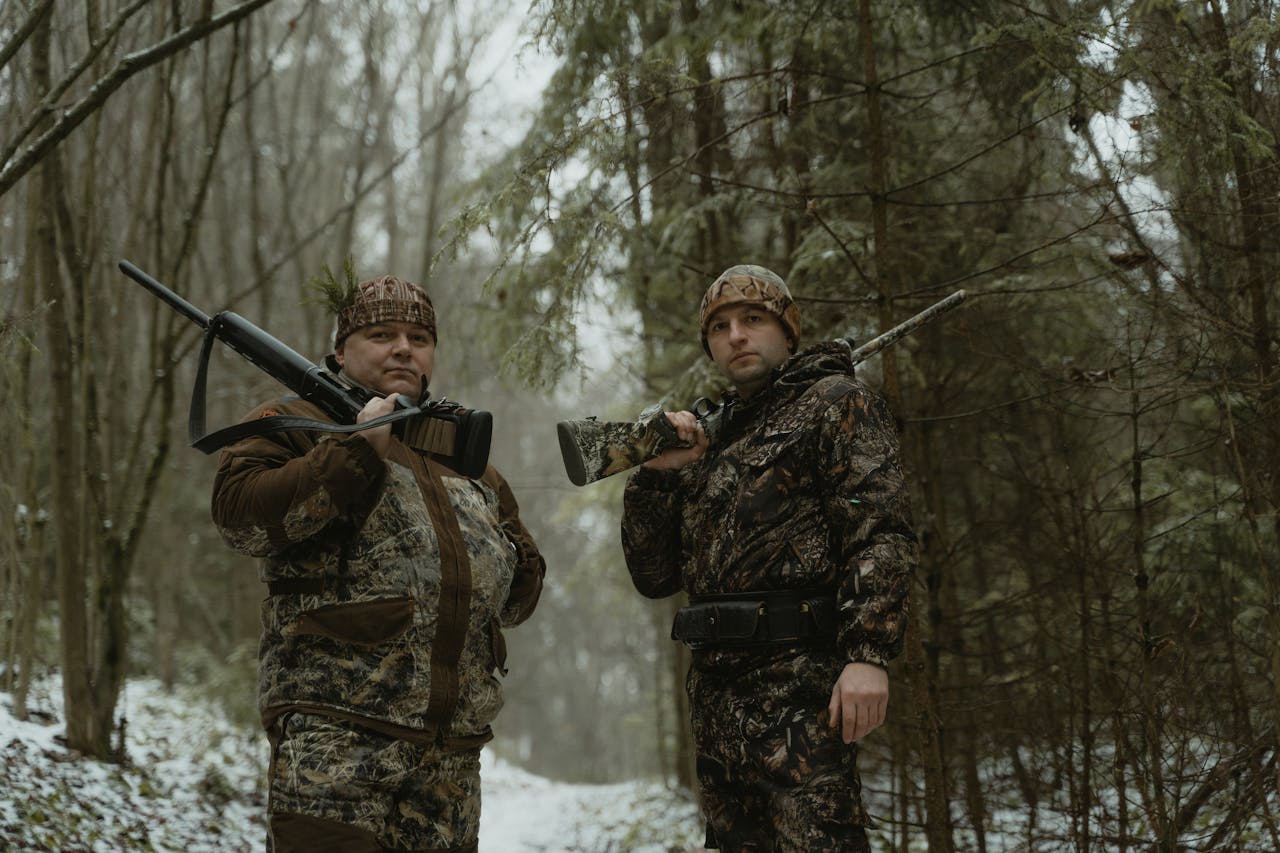 headline Two hunters in camouflage with rifles in a snowy forest landscape.