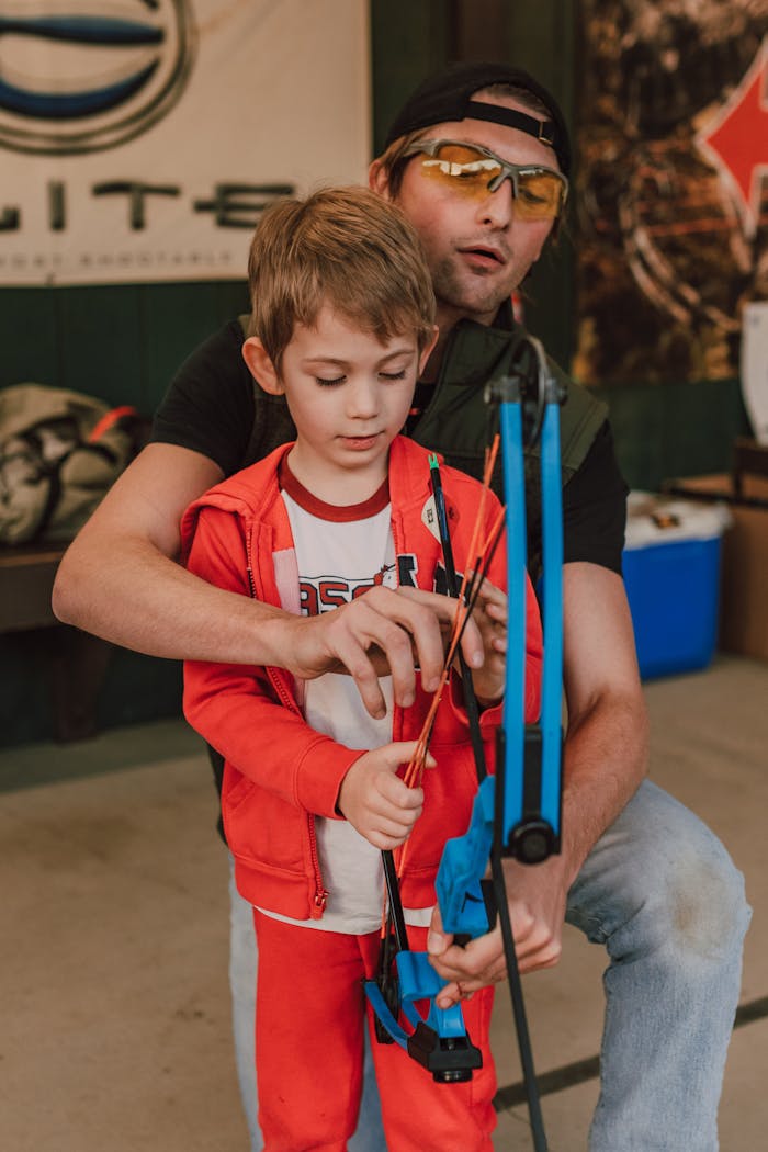 category-04 Father teaching son archery basics at an indoor range, fostering bonding and skill development.